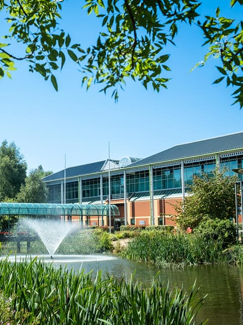 Holywell Park Conference Centre in the sunshine with a lake and fountain in the foreground.
