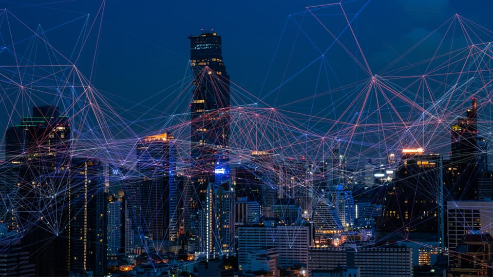 A city skyline of tall buildings at night, overlaid with geometric patterns of red and blue lines.