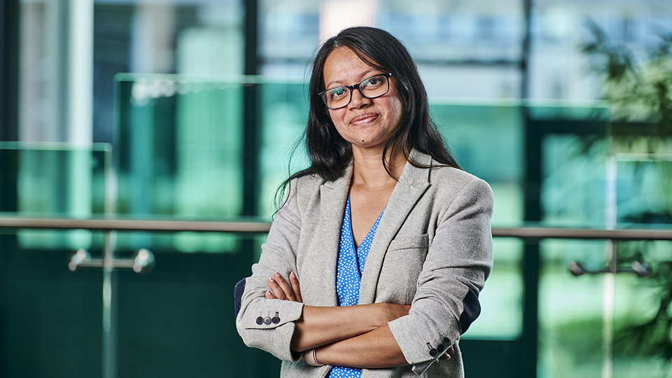 A woman with black hair wearing a light blazer posing for a professional headshot