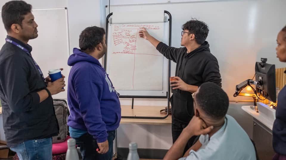 A group of students in discussion, with one of them pointing to text on a whiteboard.