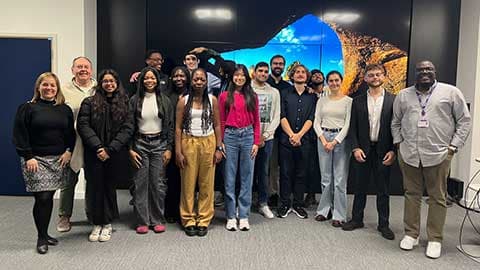 A group of students and staff standing in front of a large screen.