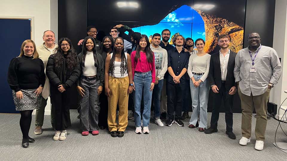 A group of students and staff standing in front of a large screen.