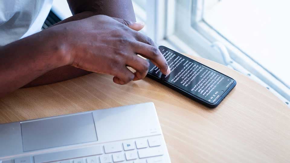 Someone scrolling on a smartphone with a laptop keyboard to the side.