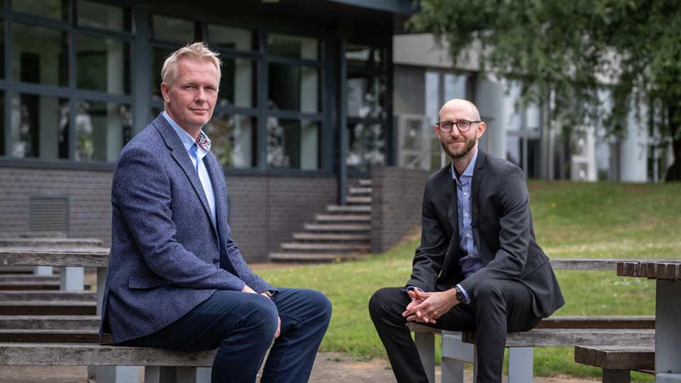 Tom Jackson and Ian Hodgkinson sitting on benches outside a building in a grassy area.