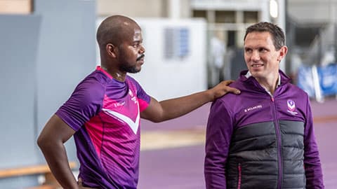 Ntando Mahlangu with his hand placed on the shoulder of a coach. They are both wearing purple Loughborough Sport attire.