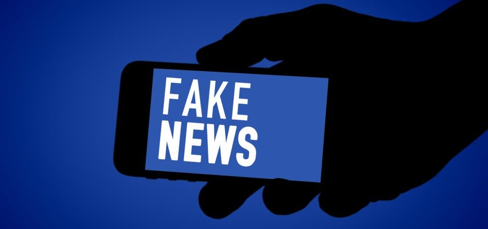 A graphic of a hand holding a smartphone that says 'fake news'.