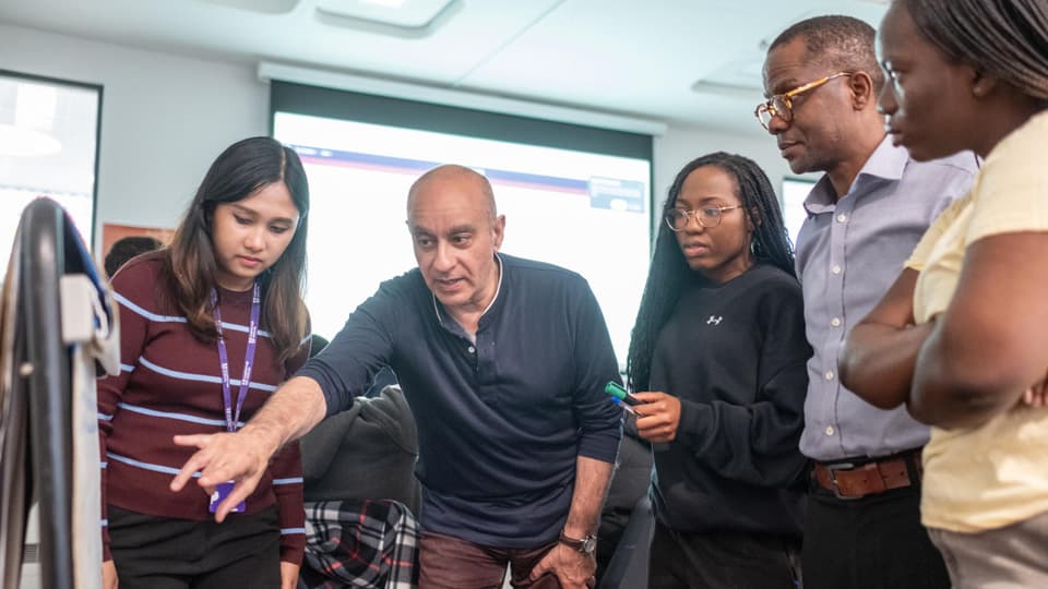 An academic demonstrates something on a flip chart to a gathering of four students.