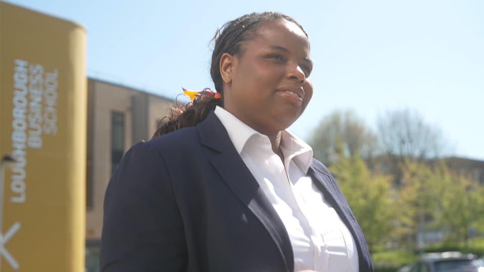 A female MBA student in a white shirt and blue jacket walking away from the Business School building.