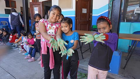 Three school children in Guatemala showing the palms of their hands which are painted green.