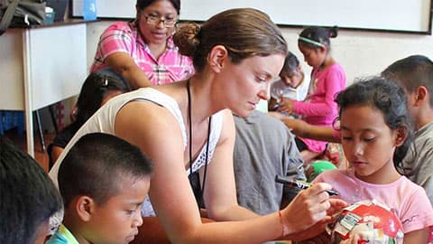 Adults helping school children glue newspaper and draw onto plastic balls.