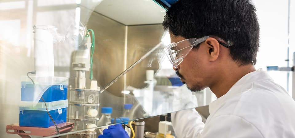 Sudarshan working in a lab wearing goggles with a glass screen
