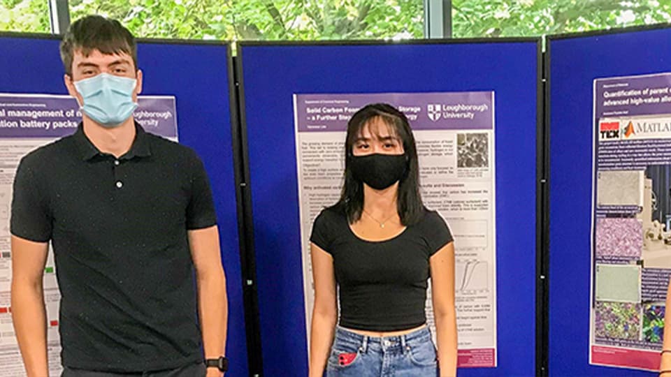 male and female students in masks in front of their posters