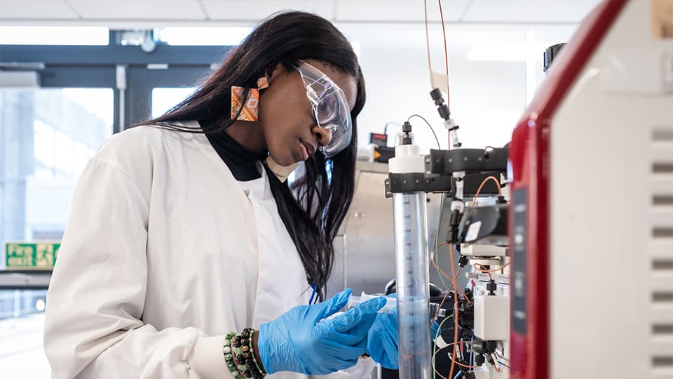 student working in a lab wearing a lab coat and goggles