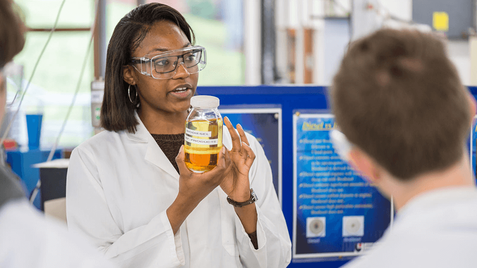 1 black female student holding a bottle of solution showing to students