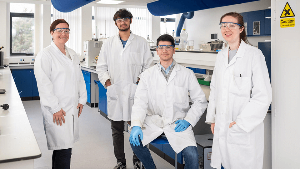 4 students (male and female) in lab coats in a lab 