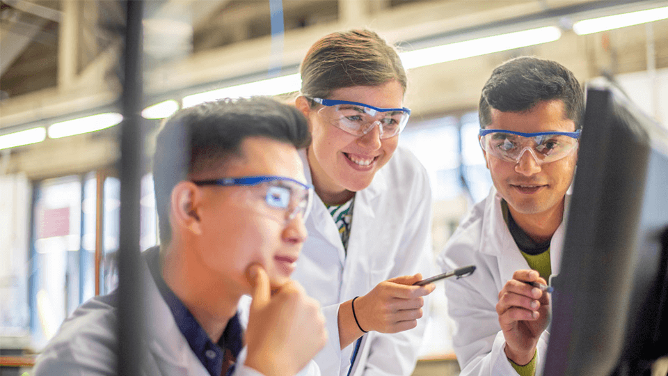 3 students (1 female and 2 male) in a lab looking at a screen