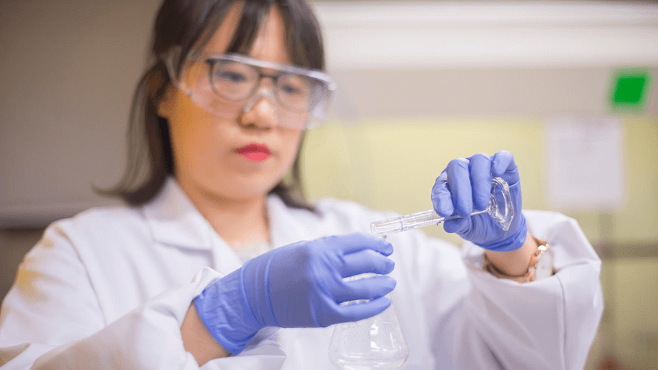 female student wearing goggles holding a beaker