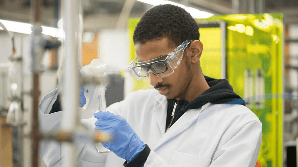 male student in lab coat pouring solution into a beaker