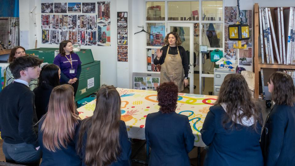 Teacher stands around a table talking to students sitting down