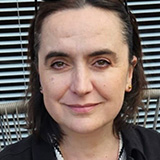 Natalia Valdivieso wearing a dark jacket standing in front of a stiped background