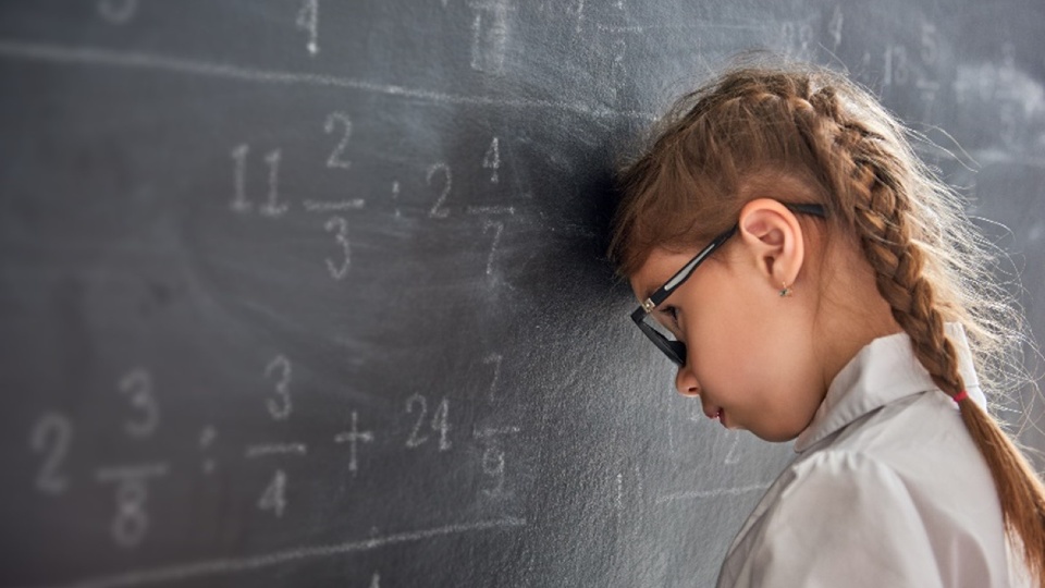 A young girl face a black board with numbers on it with her head against it.