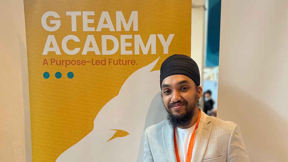 Headshot of student standing in front of a banner that reads 'G- Team Academy - a purpose-led future'.