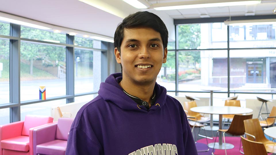 Student Rohit, standing the Wolfson School foyer, smiling at the camera, wearing purple Loughborough University hooded jumper. 