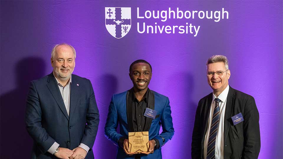 Nick Jennings, a student and Professor Michael Henshaw, standing in front of a purple background together, smiling whilst looking at the camera.