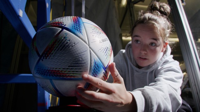 Close-up of a student placing a football into a piece of testing equipment. 