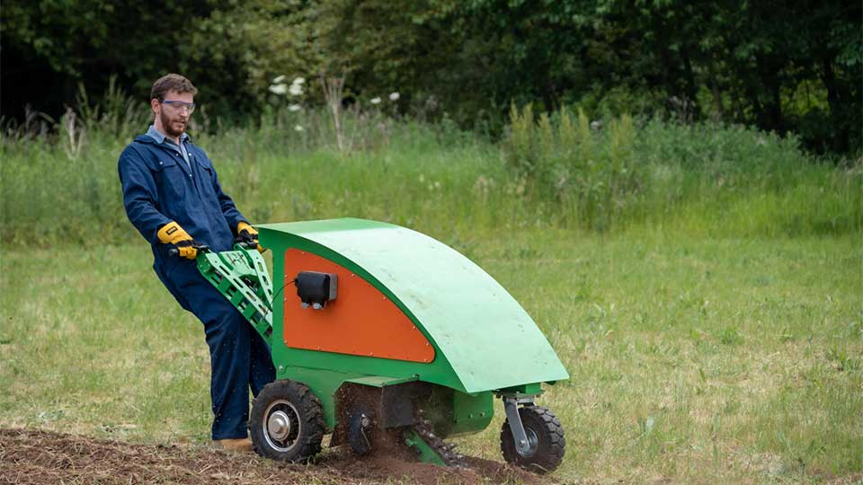 An academic pushing a solar micro tractor in a field