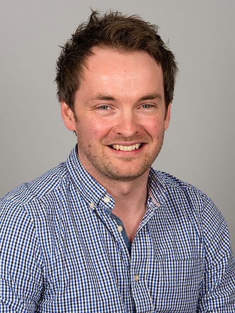 Headshot of Jake, smiling with a grey background