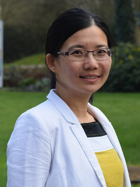 Headshot of Dr Mey Goh from a side profile, smiling whilst looking directly at the camera. 