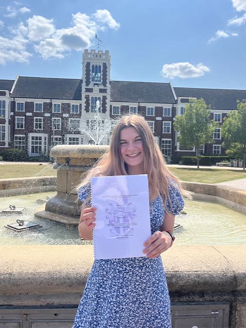 Izzy holding a certificate in front of the University campus