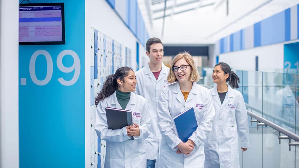 A group of four students in white lab coats walking down the central corridor of the STEMLab facility.