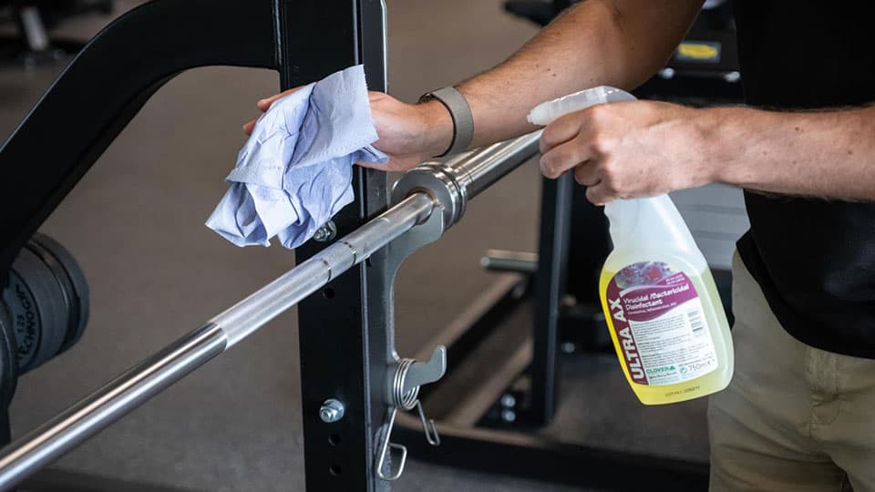 Someone cleaning gym equipment with a paper towel and disinfectant spray