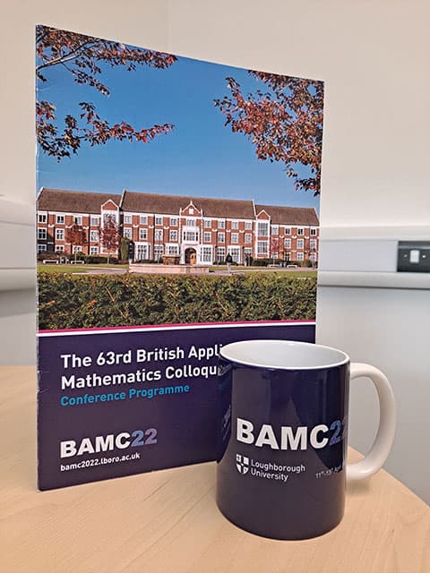 A photograph of the BAMC 2022 mug with a conference programme stood behind it