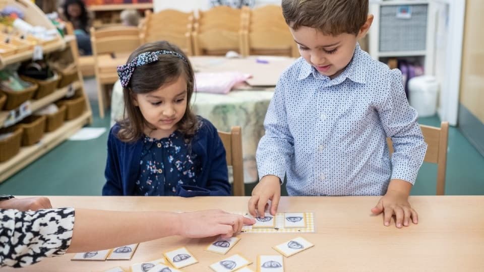two children playing a card game with the teacher