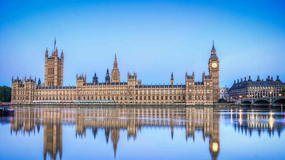 A photograph of the UK's houses of parliament, reflecting against the River Thames.
