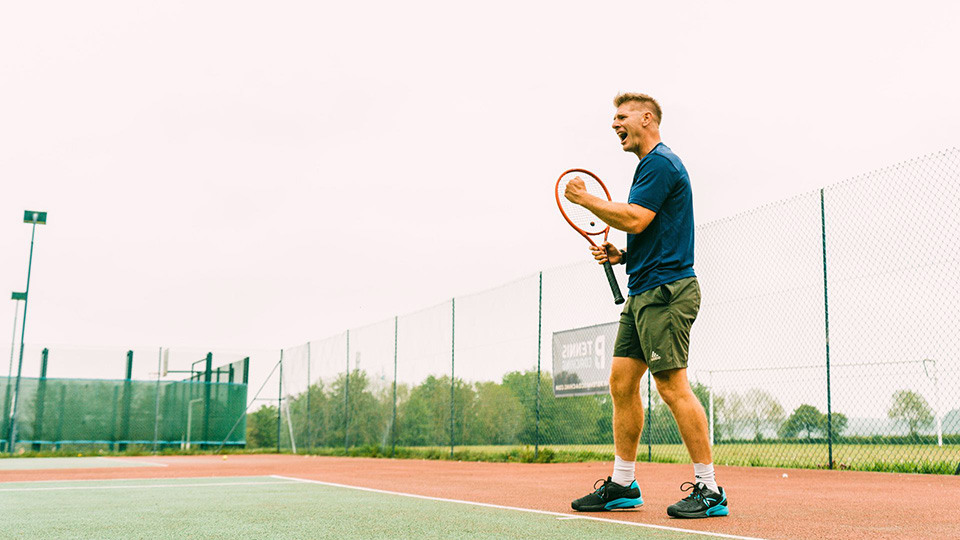 man on tennis court with tennis racket in hand, celebrating winning a match