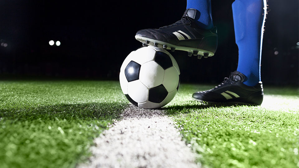 a close up of a person wearing football boots standing with one foot on top of a football