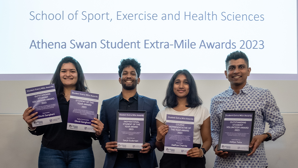 some athena swan student extra mile award winners stood at the front of a lecture theatre holding their certificates and smiling to camera