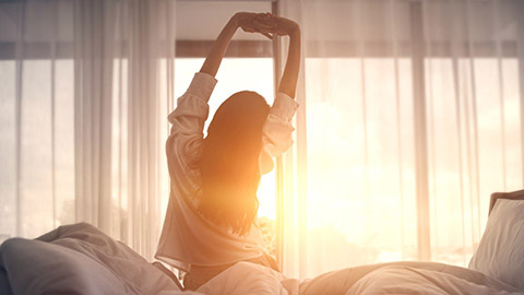 Lady stretching after waking up with sun streaming in the window