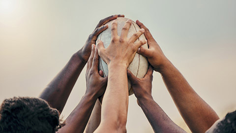 Hands on a rugby ball. Image provided by Getty.