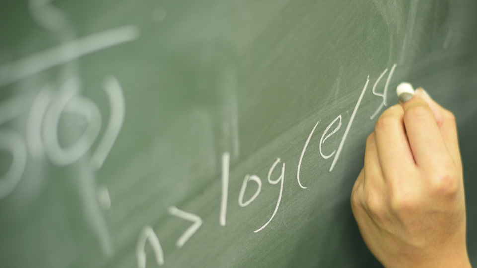 a hand holding chalk and formula on a chalk board