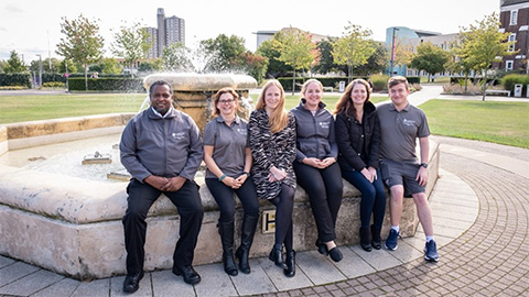 smiling wardens sat around Hazlerigg fountain wearing their university uniform