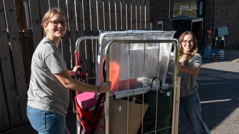 Two Fresher Helpers with a luggage trolley outside Royce Hall, assisting new students with their move-in.