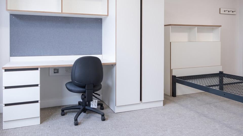 A neatly arranged bedroom showcasing a bed, a desk, and a cabinet