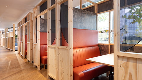 Study spaces with private comfy booths and wooden tables inside common room spaces in Loughborough London University Stratford One accommodation. The booths are divided by wooden beams, and inside each booth is a large table for studying and comfy orange sofas with views of London.