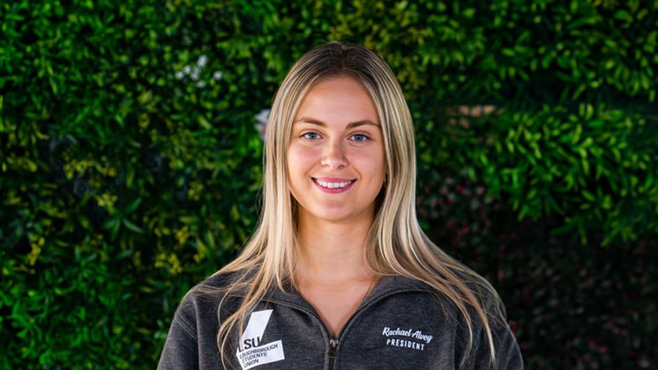 The LSU president Rachael Alvey smiles towards the camera and wears a Loughborough Student Union branded hoodie.