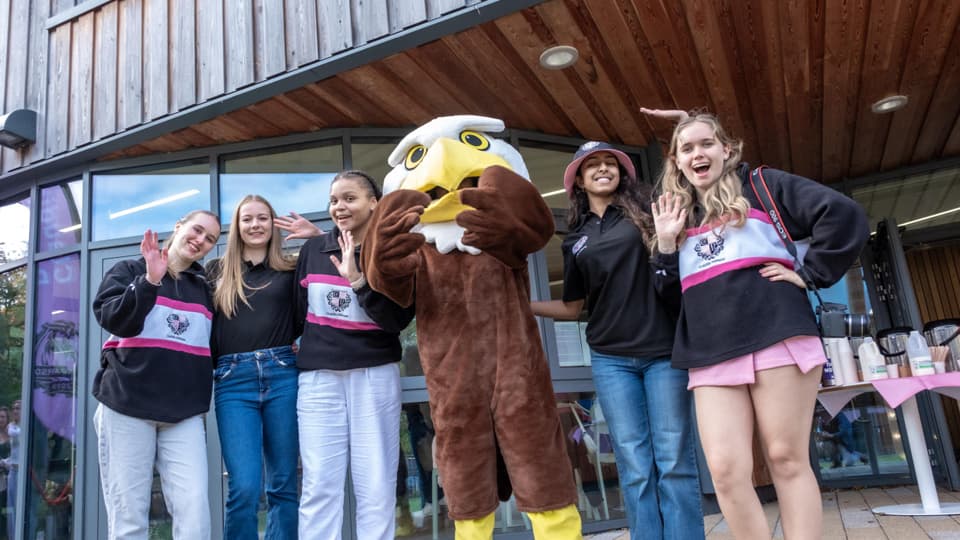 Student posing for a photo outside of claudia parsons with their hall mascot